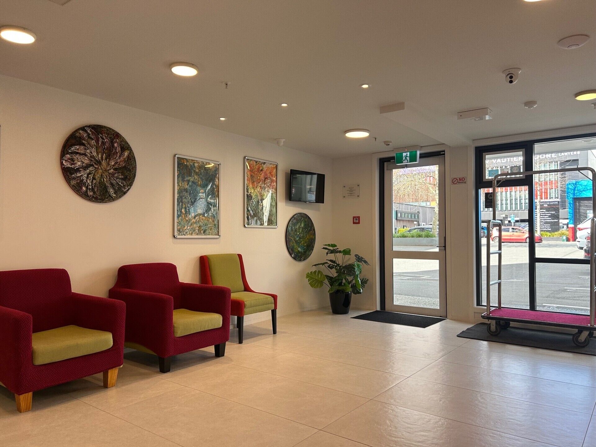 A reception area with three red chairs, a potted plant, and artwork on the wall.