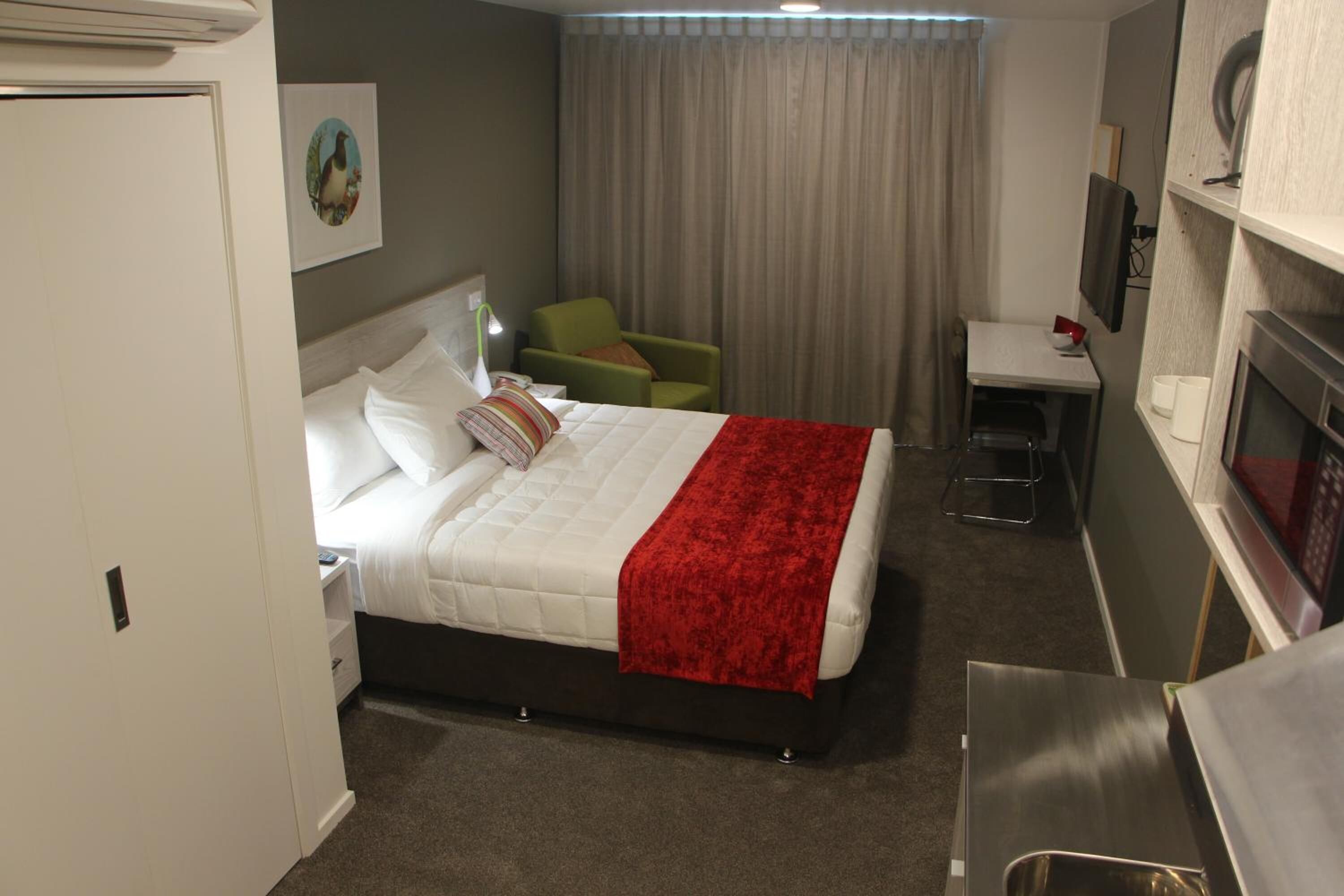 A hotel room with a bed, a desk, a chair, a TV, and a microwave.