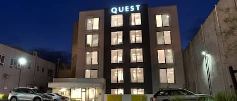 A multi-story building with the sign 'QUEST' at the top, featuring a modern design with multiple windows and a flat roof.