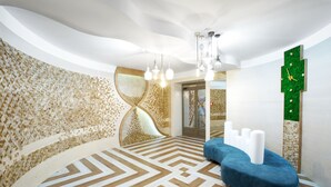 Una habitación moderna con piso de diseño geométrico, un sofá azul, un reloj de pared verde y un diseño de techo único.
