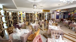 Un restaurante con varias mesas dispuestas, cubiertas con manteles blancos, sillas doradas y una variedad de botellas de vino en estanterías.