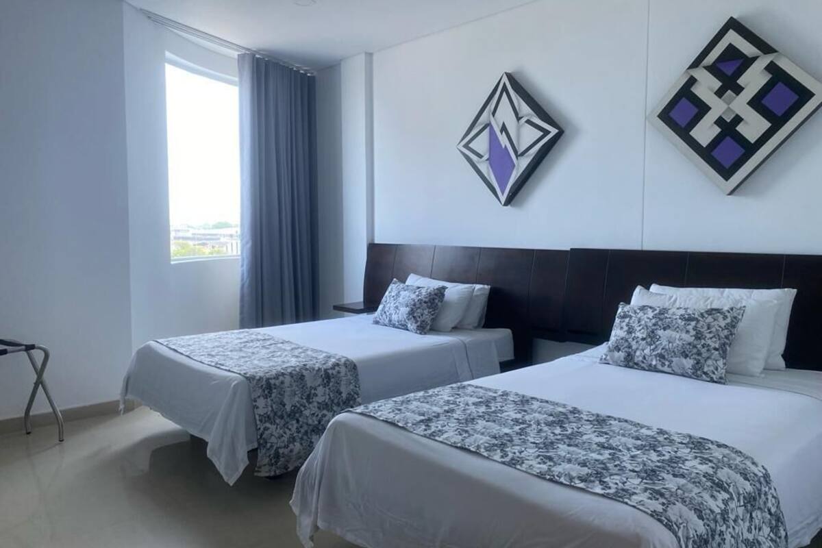 A hotel room with two beds, a window with curtains, and two wall art pieces.