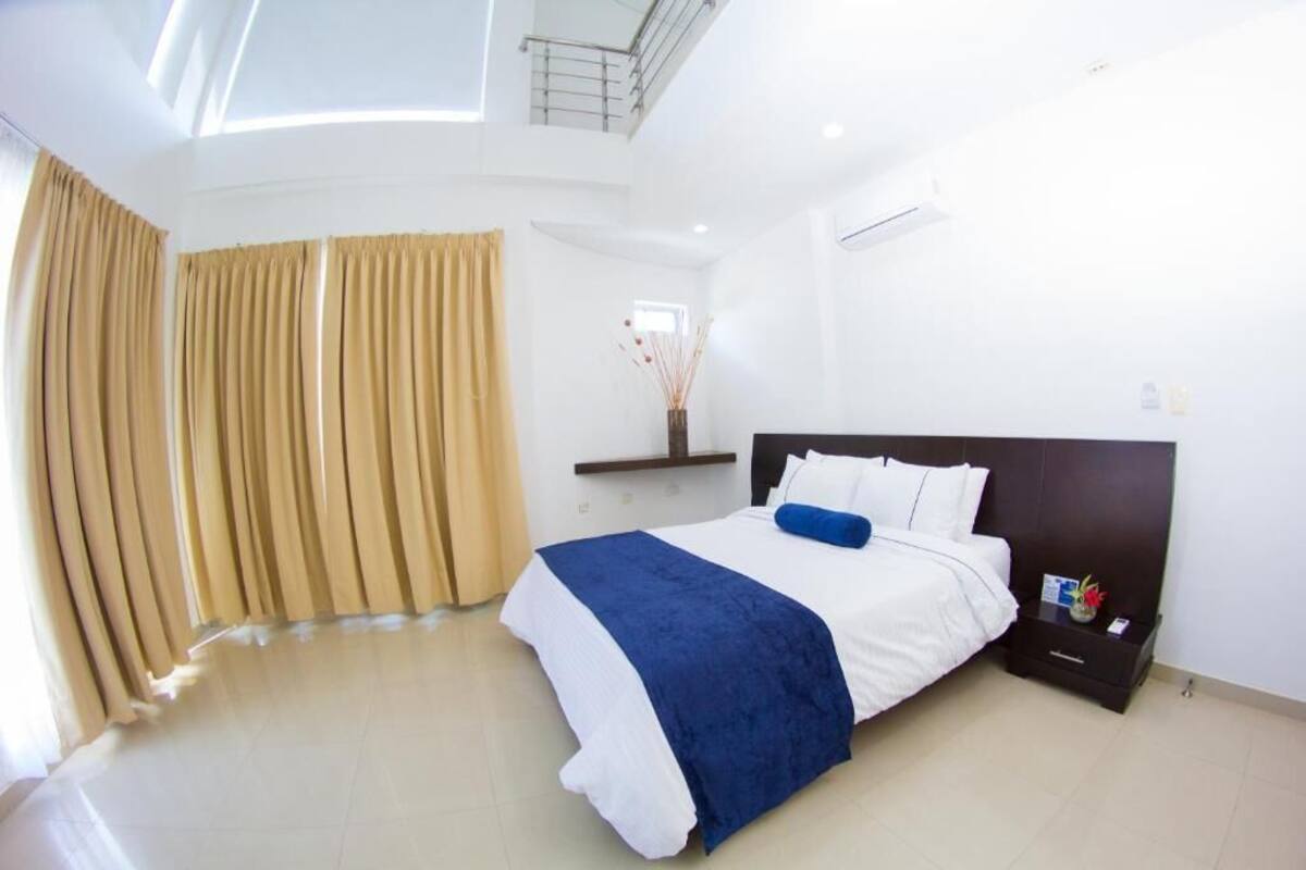 A bedroom with a large bed, a nightstand, a window with curtains, and a skylight.