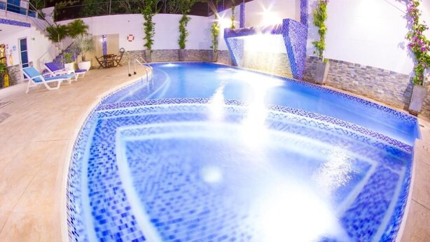 A swimming pool with a water feature, surrounded by lounge chairs and potted plants. - Hotel Altamar (Cartagena)