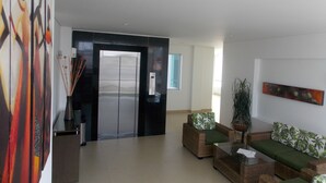 A modern lobby with a reception desk, a waiting area with sofas and a coffee table, and a large elevator. - Hotel Altamar (Cartagena)