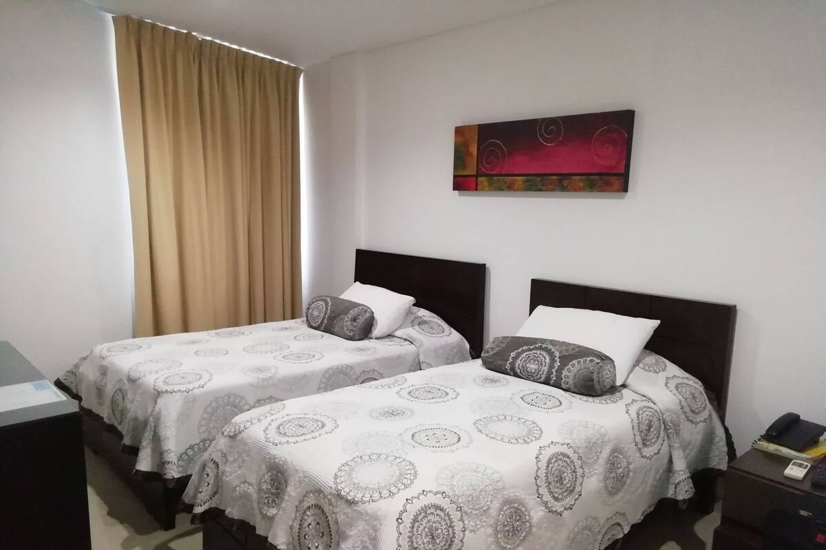 A hotel room with two beds, a desk, a nightstand, and a painting on the wall.