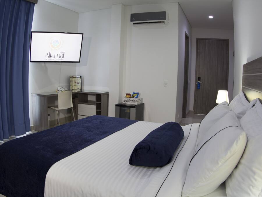 A hotel room with a bed, a desk, a TV, and an air conditioning unit.