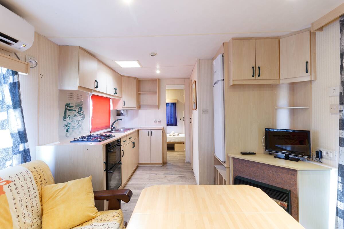 A compact kitchen with a stove, sink, and refrigerator, a dining area with a table and chairs, and a small TV on a stand.