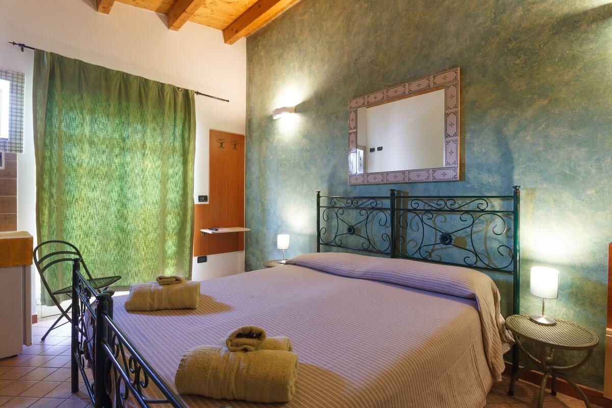 A bedroom with a bed, two bedside tables with lamps, a green curtain, and a mirror on the wall.