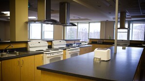 A kitchen with wooden cabinets, a stove, a toaster, and a window providing natural light. - Grenfell Campus Summer Accommodations (Corner Brook)