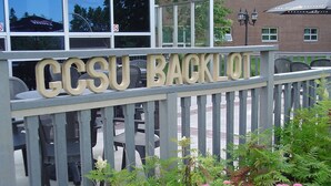 A sign with the text "GCSU BACKLOO" on a fence, surrounded by greenery and outdoor seating. - Grenfell Campus Summer Accommodations (Corner Brook)