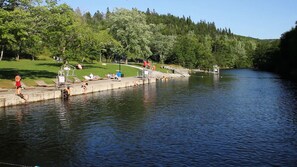 Un parque junto al río con un embarcadero de hormigón, sillas de descanso y una zona verde.