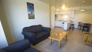 A living room with a sofa, a coffee table, and a kitchen area with a microwave and cabinets. - Grenfell Campus Summer Accommodations (Corner Brook)