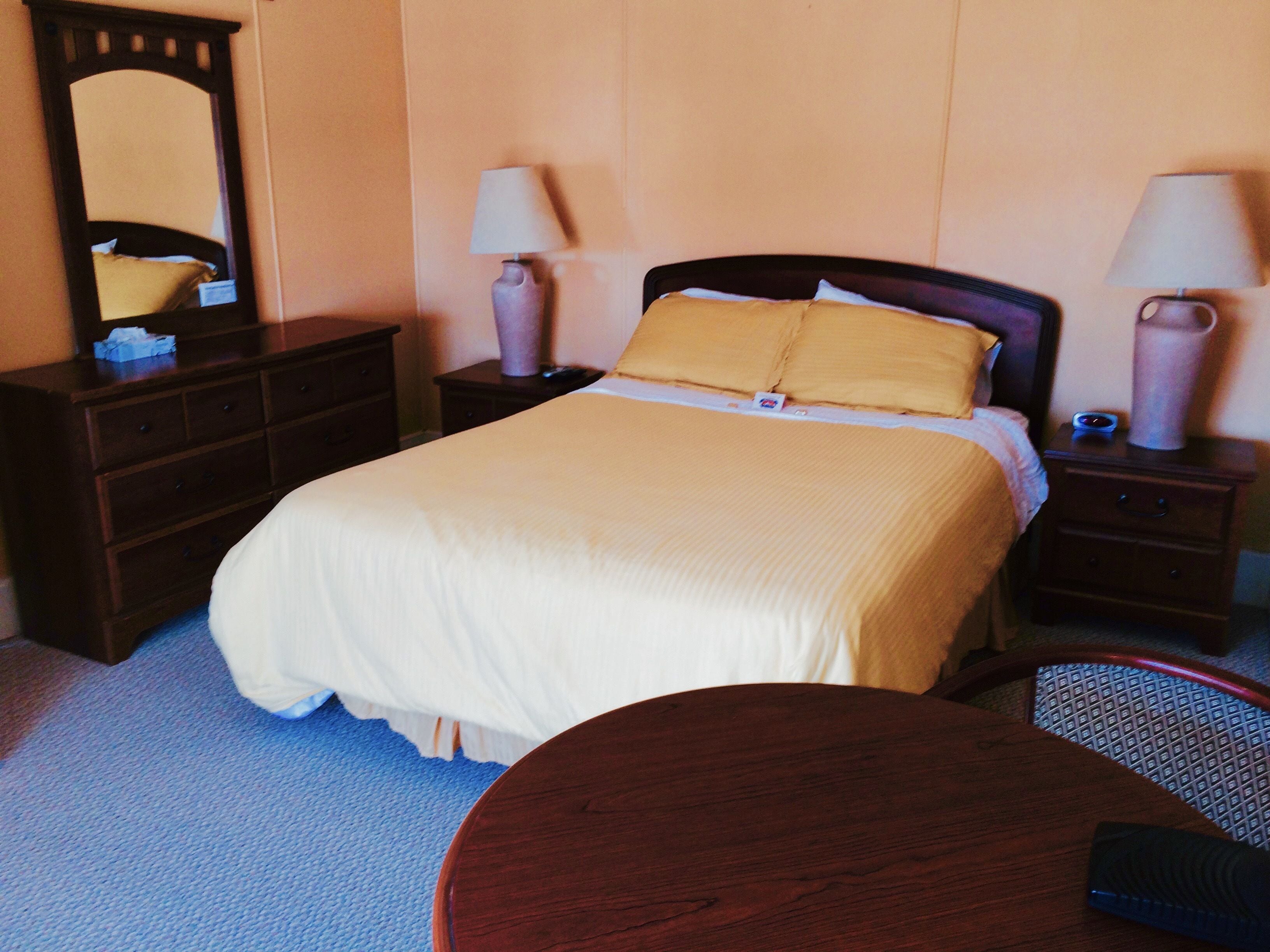 Una habitación de hotel con una cama, dos mesitas de noche con lámparas, un aparador y una mesa redonda.
