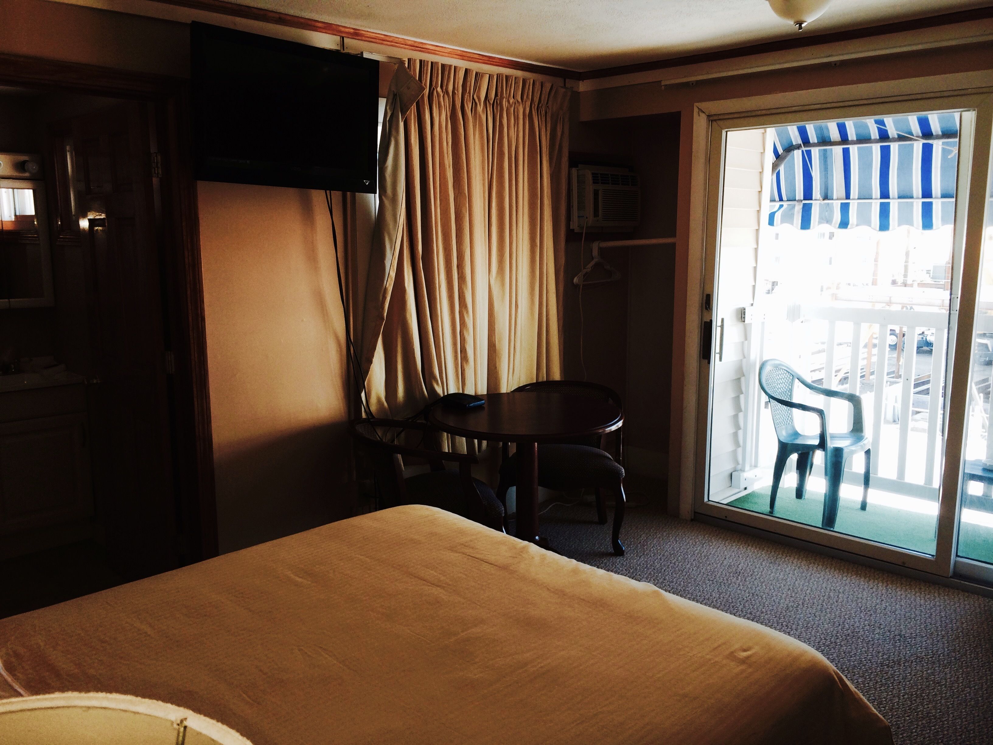 Habitación de hotel con una cama, una mesa con dos sillas, televisión y un ventanal corredero que da a un área exterior.