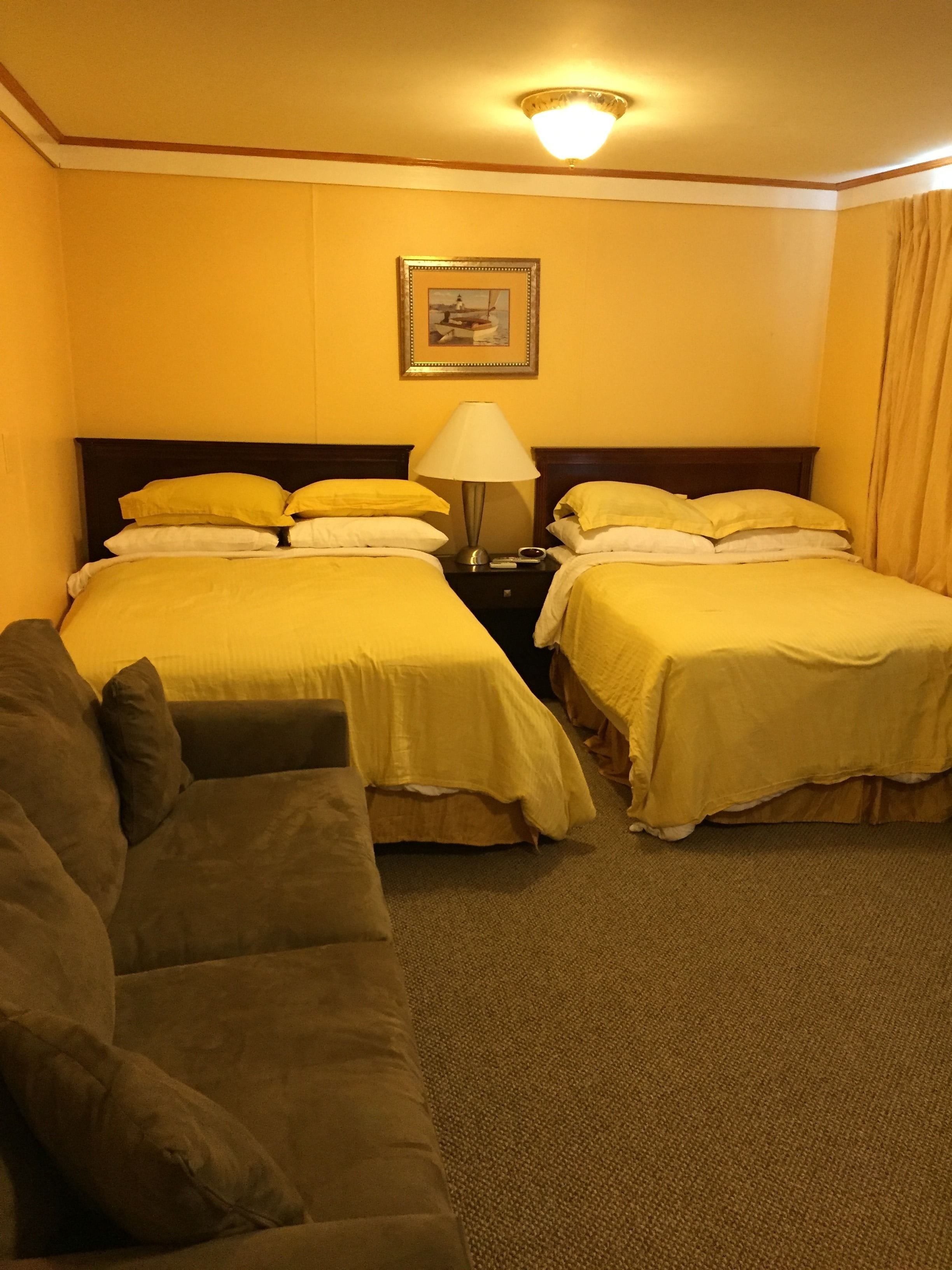 A hotel room with two beds, a nightstand, a lamp, and a sofa.