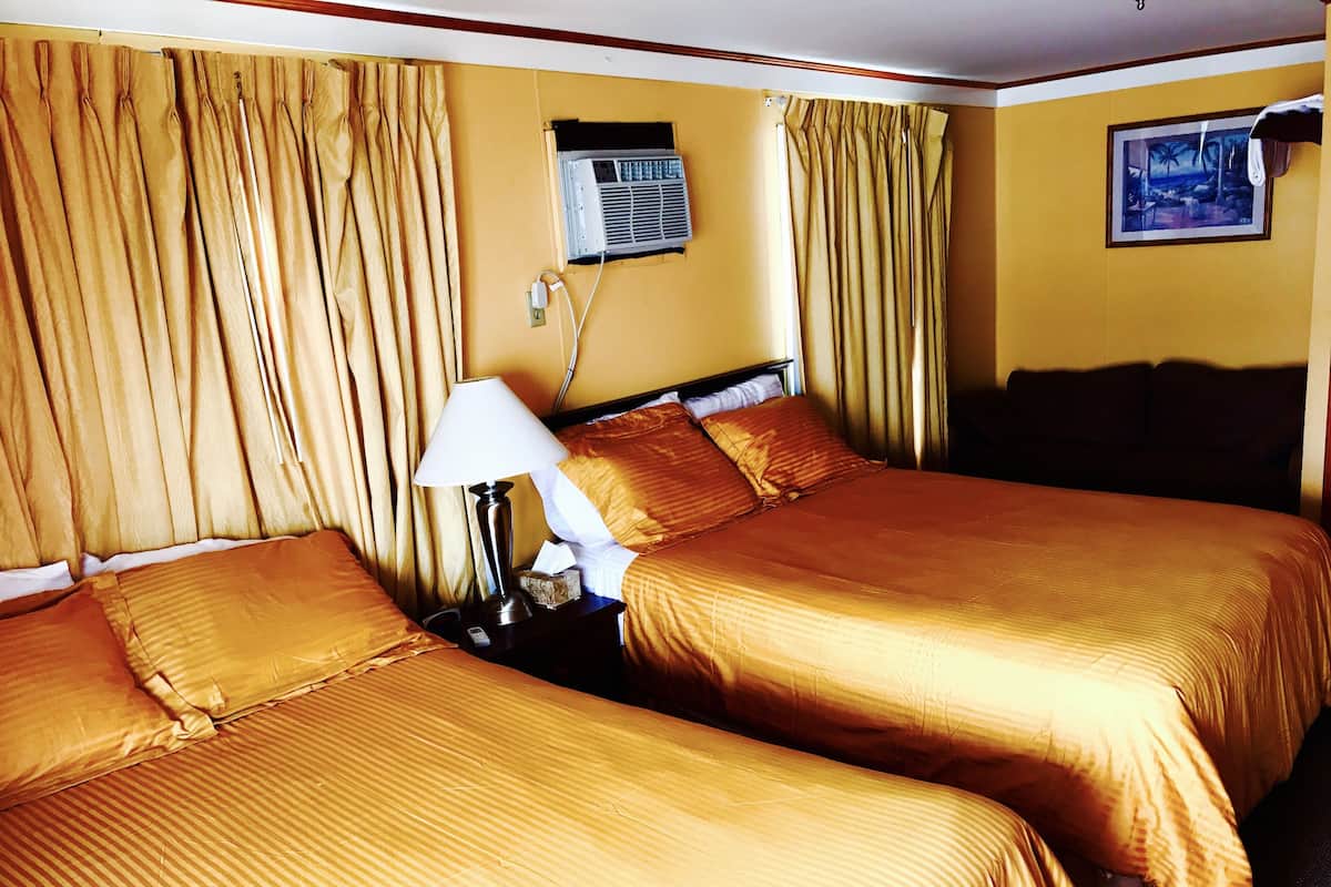 Een hotelkamer met twee bedden, een nachtkastje met een lamp, een airconditioning en een schilderij aan de muur.