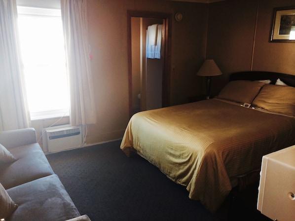 A hotel room with a bed, a nightstand, a lamp, a window with curtains, and a wall-mounted picture. - Moulton Hotel (Hampton)