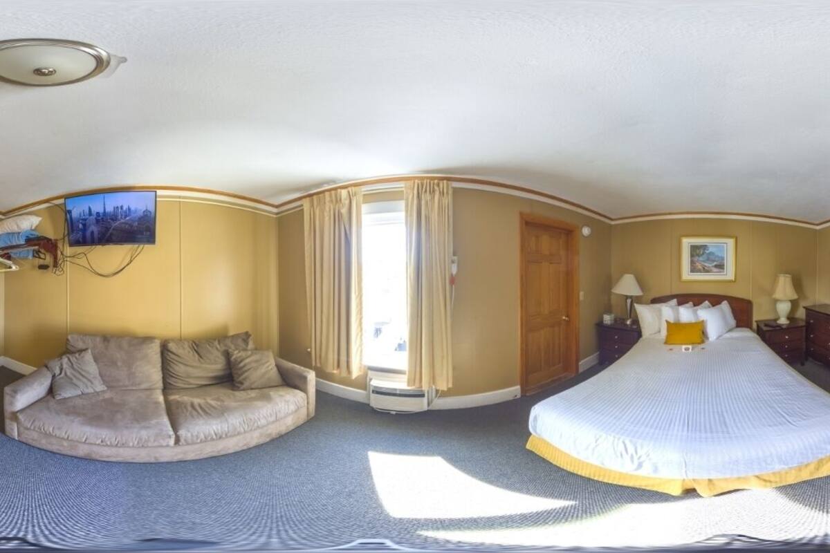 Een hotelkamer met een gebogen plafond, een bank, een bed en een groot raam met gordijnen.