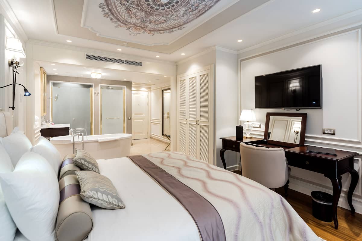 Quarto de hotel com uma cama grande, uma escrivaninha, uma cadeira, uma televisão e um banheiro com chuveiro e vaso sanitário.