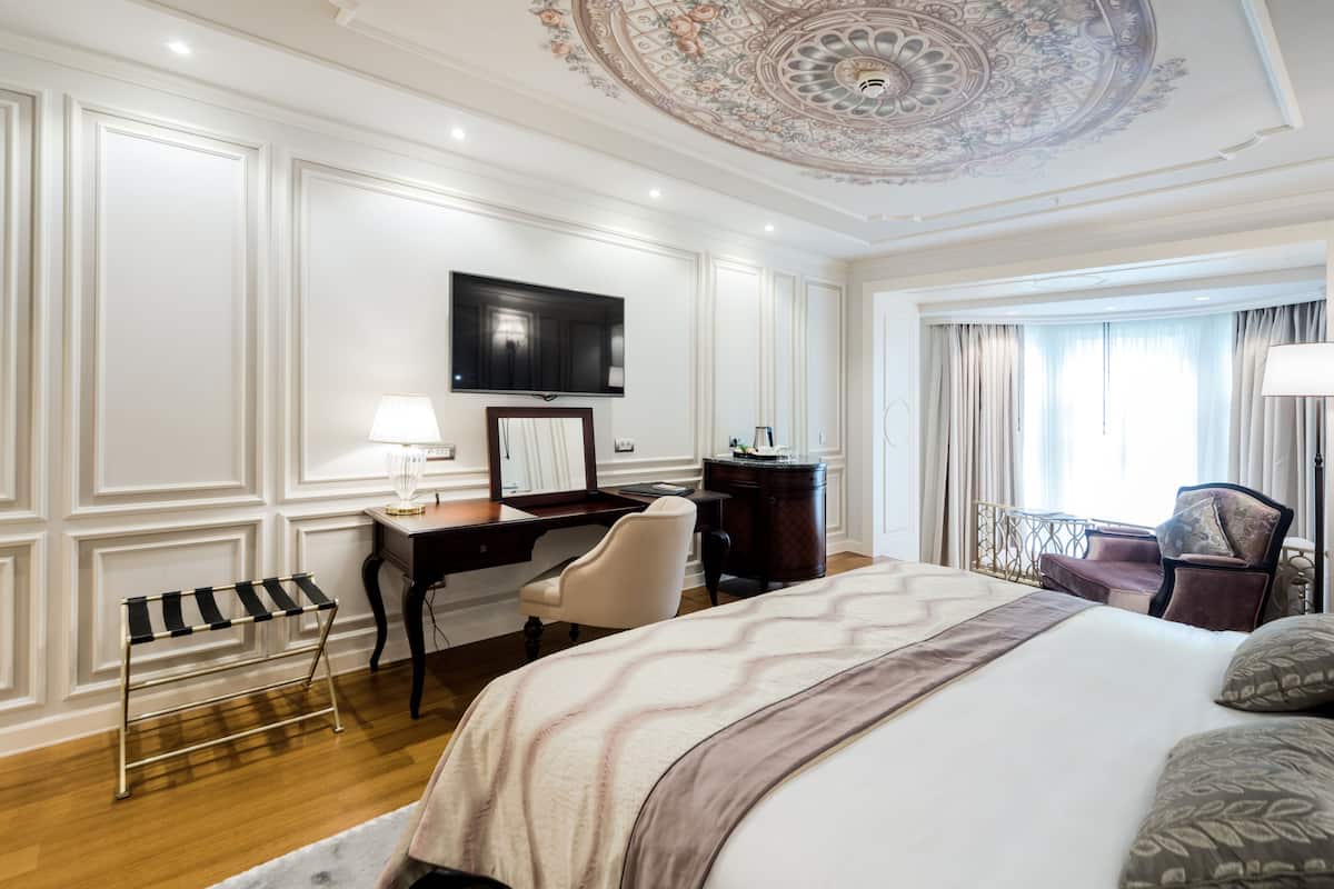 Quarto de hotel com uma cama grande, uma escrivaninha com cadeira, televisão e janela com cortinas.