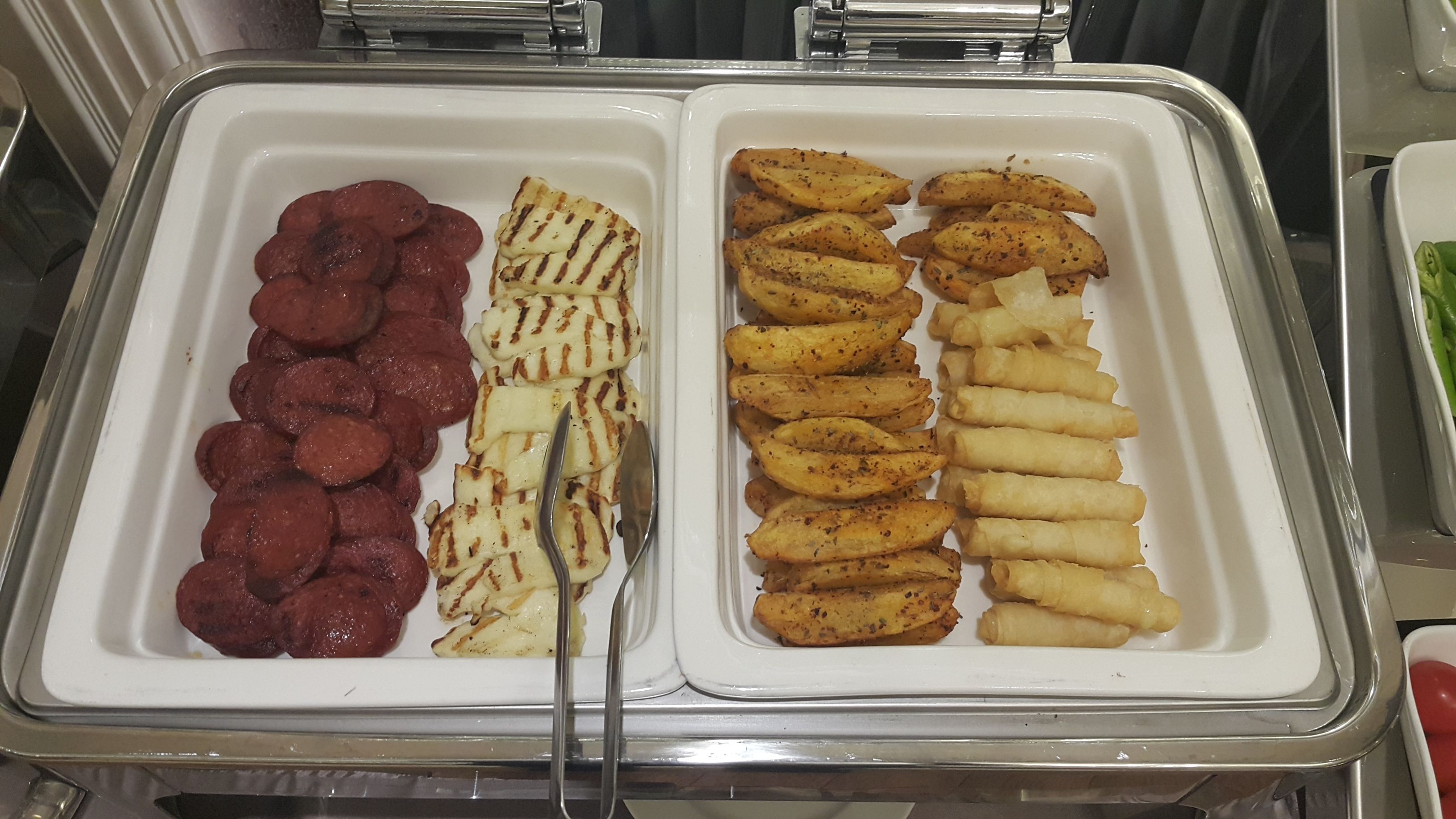 Un bufé con salchichas en rodajas, papas a la parrilla y rollitos de primavera fritos.
