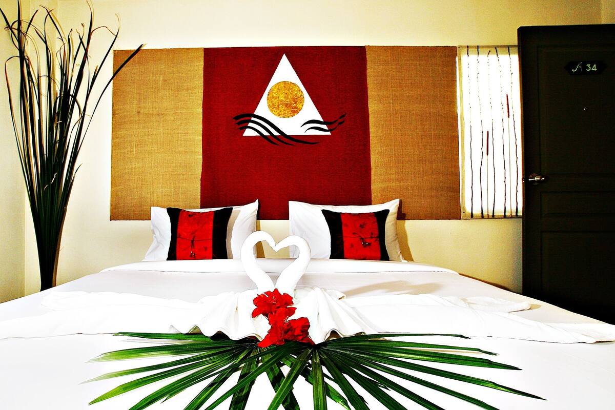 A hotel room with a bed, a wall tapestry, a door, and a plant.