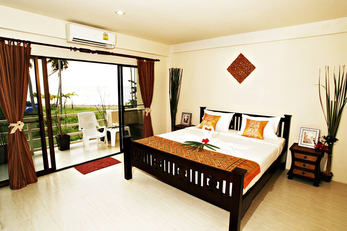 A bedroom with a bed, a nightstand, a potted plant, and a view of the outdoors.