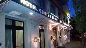 A hotel with a sign reading "HOTEL GEO" and a well-lit entrance with potted plants. - Hotel Geo (Rome)