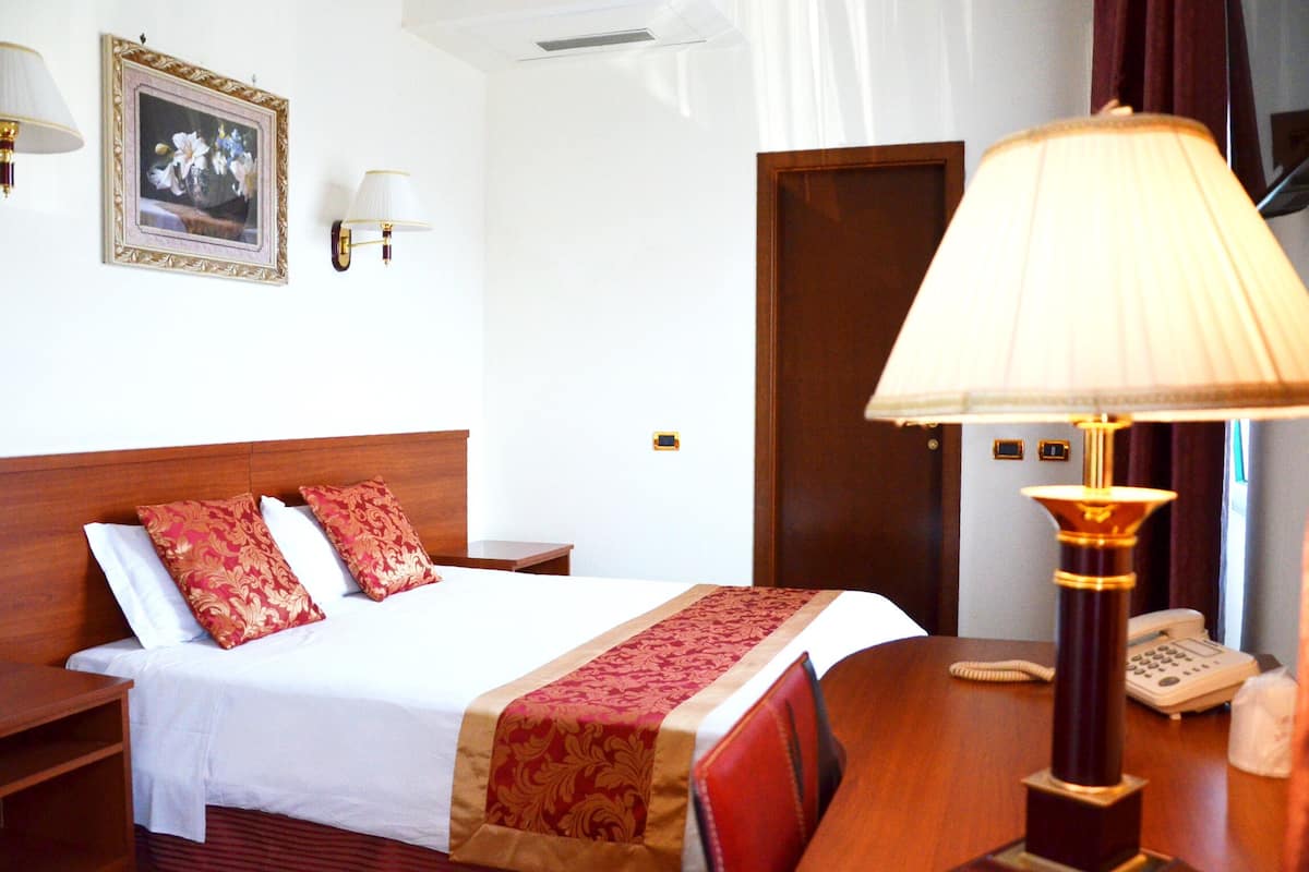 Une chambre d’hôtel avec un lit, un bureau, un téléphone et une lampe.