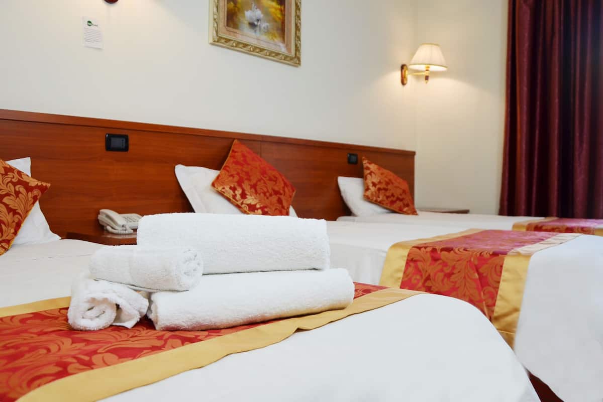 Une chambre d’hôtel avec deux lits, chacun recouvert de draps blancs et d’une courtepointe à motifs rouges. On trouve des serviettes pliées sur les lits, une table de chevet avec un téléphone et une lampe fixée au mur.