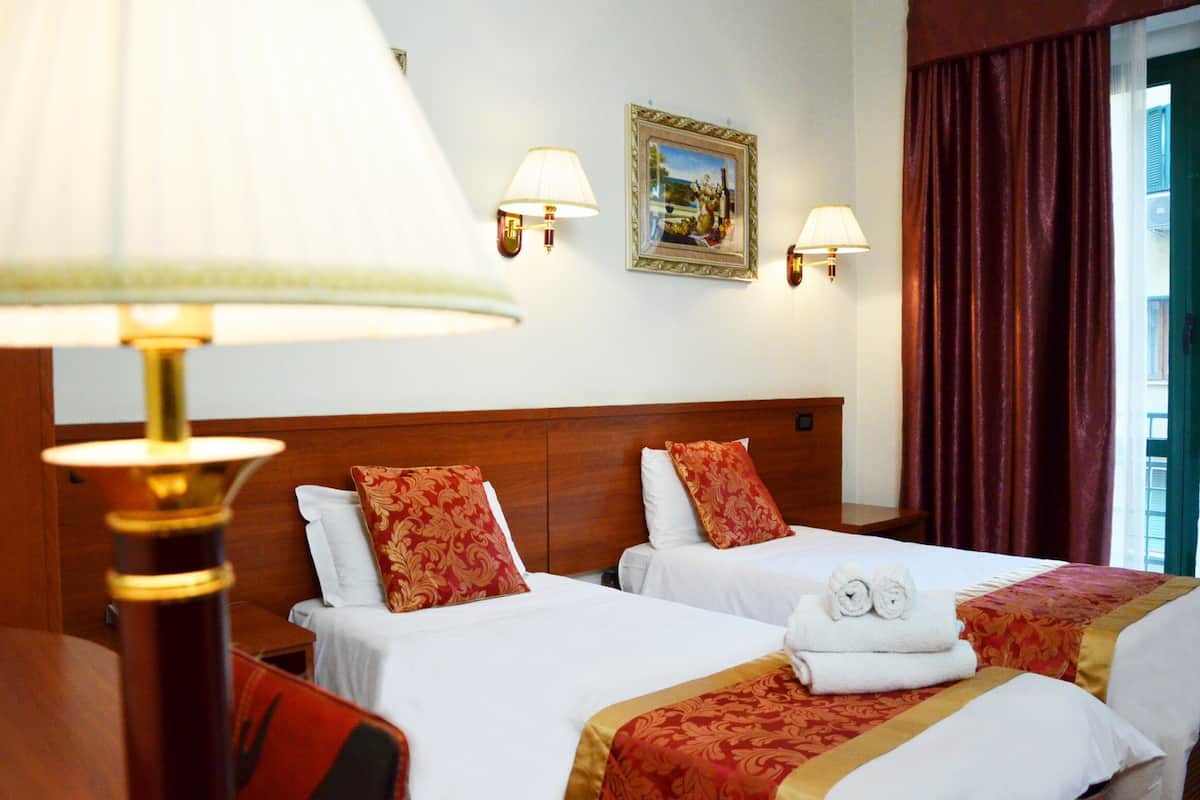 Une chambre d’hôtel avec deux lits, une tête de lit en bois, des lampes fixées au mur et un tableau encadré.