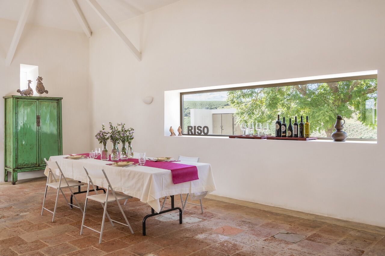 A dining area with a table set for four, a green cabinet, and a window with bottles and a vase.