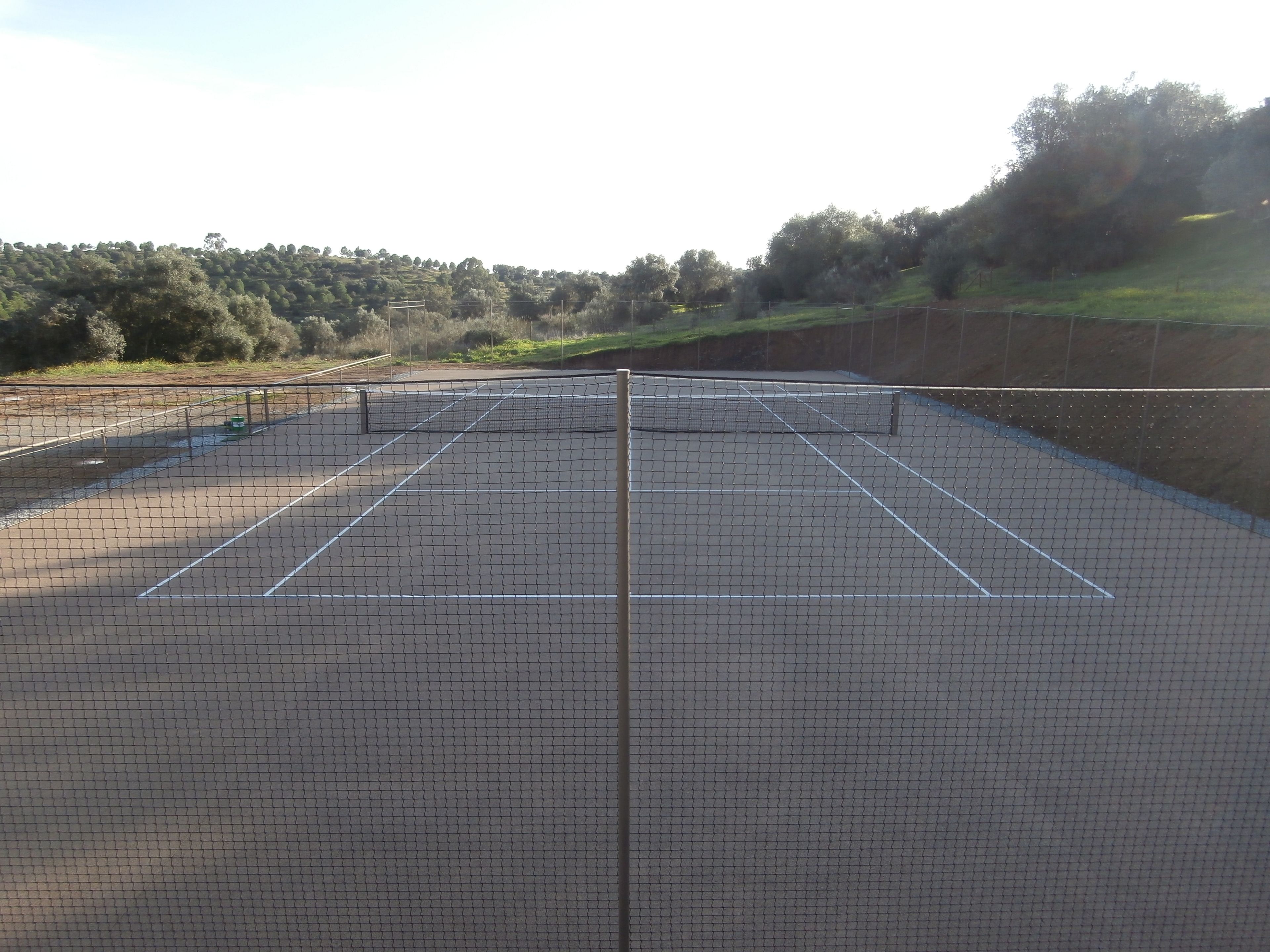 A tennis court with a net, surrounded by a fence and trees.