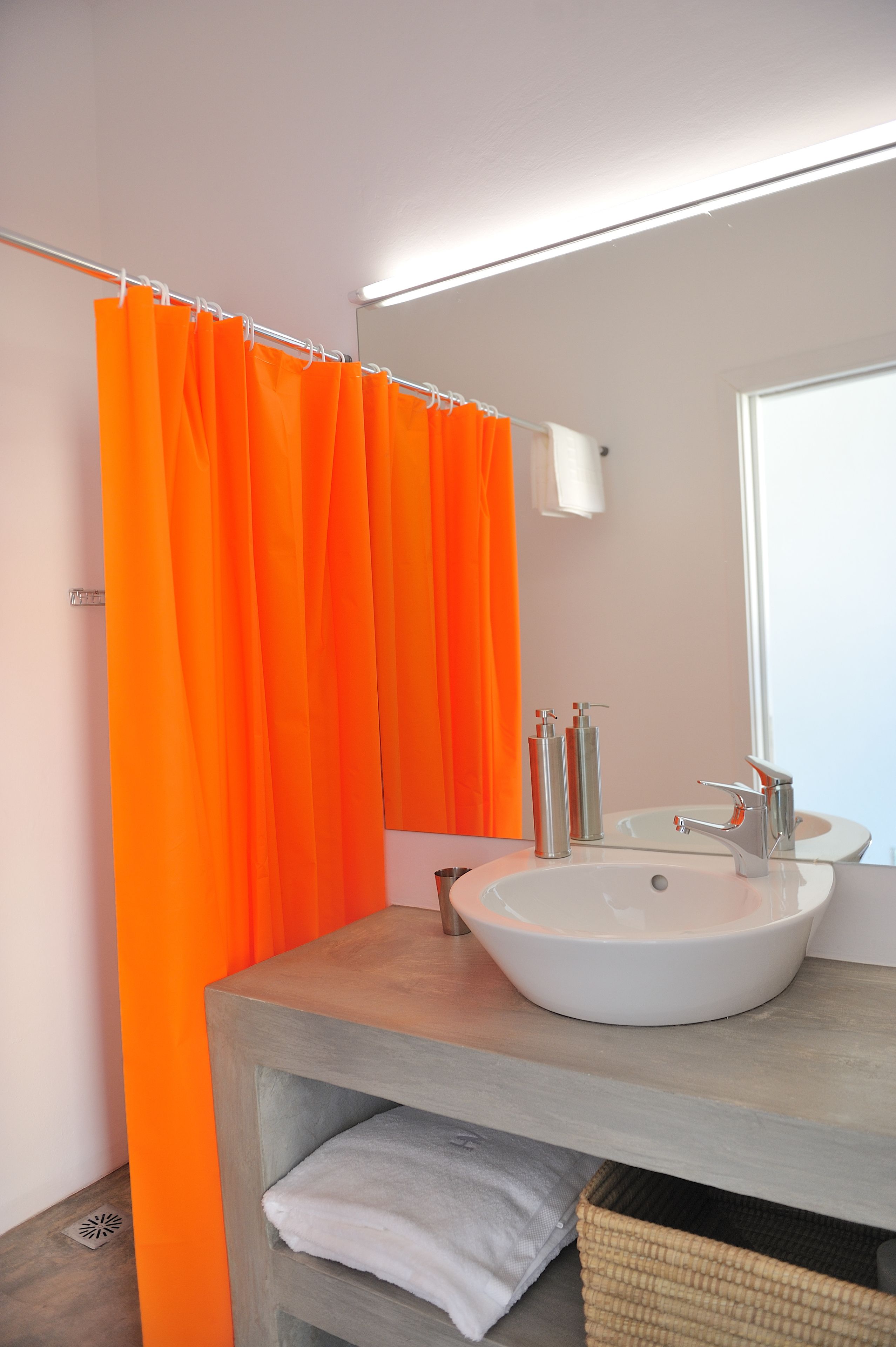 Un baño con lavamanos blanco, espejo y cortina de ducha naranja.
