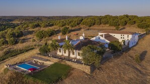 Una casa grande con piscina, rodeada de árboles y colinas.