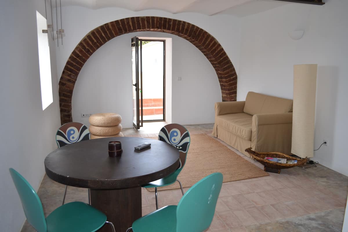 A dining area with a round table, four chairs, a sofa, and a brick archway.