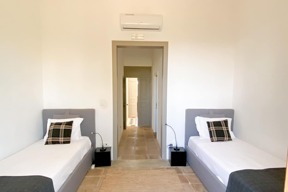 A room with two single beds, a hallway, and an air conditioning unit on the wall.
