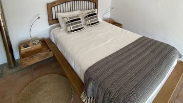 A neatly made bed with a wooden headboard, a patterned throw blanket, and a woven rug on a tiled floor.