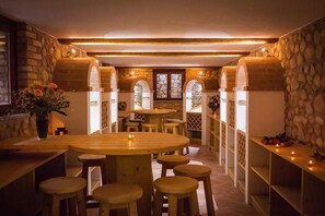 Un coin repas chaleureux avec des murs en pierre, des tables en bois et des tabourets.