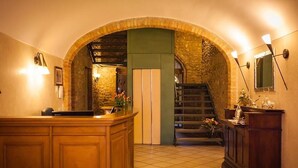 A hotel lobby with a wooden reception desk, a stone archway, a staircase, and a green wall.