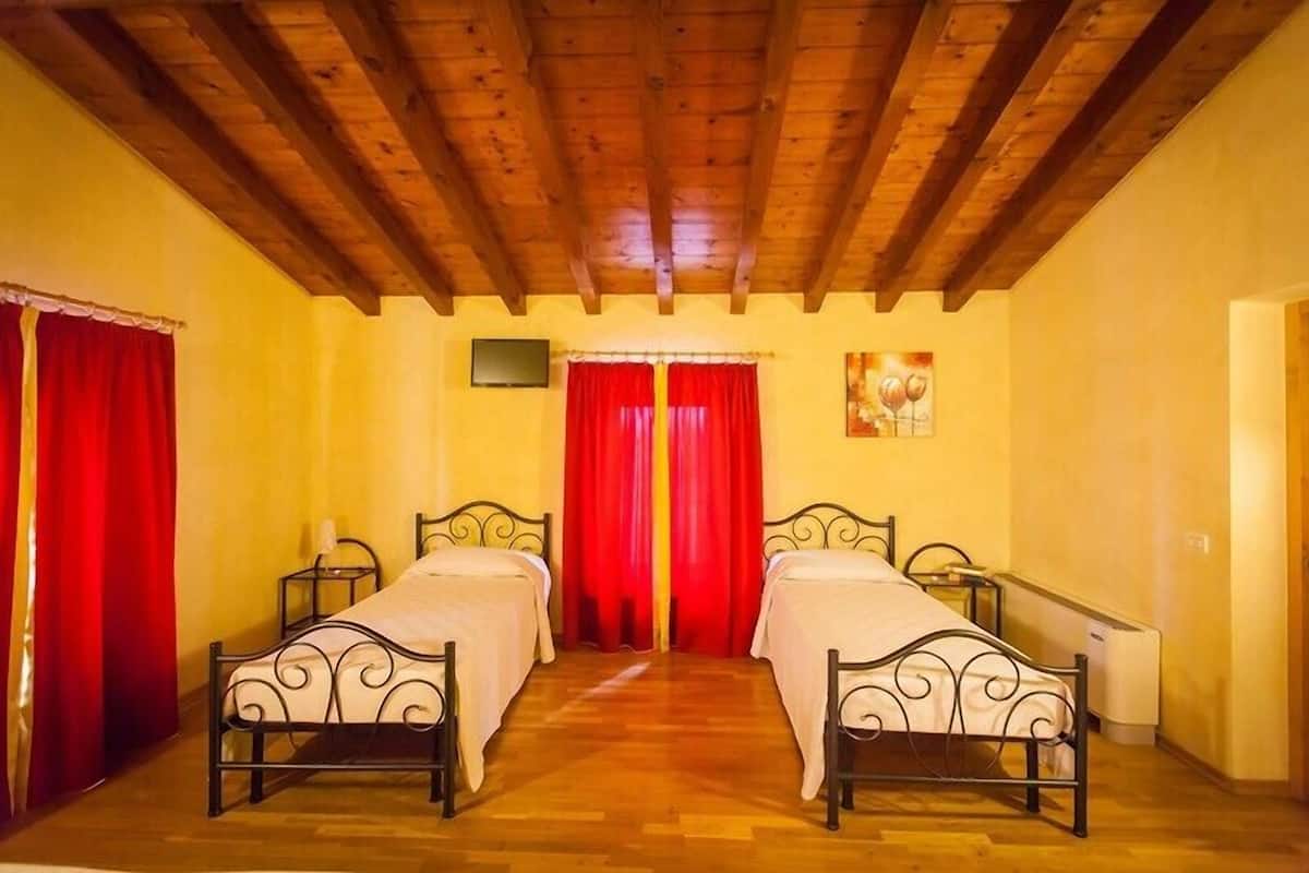 Una habitación con dos camas, vigas de madera en el techo, cortinas rojas y un cuadro en la pared.