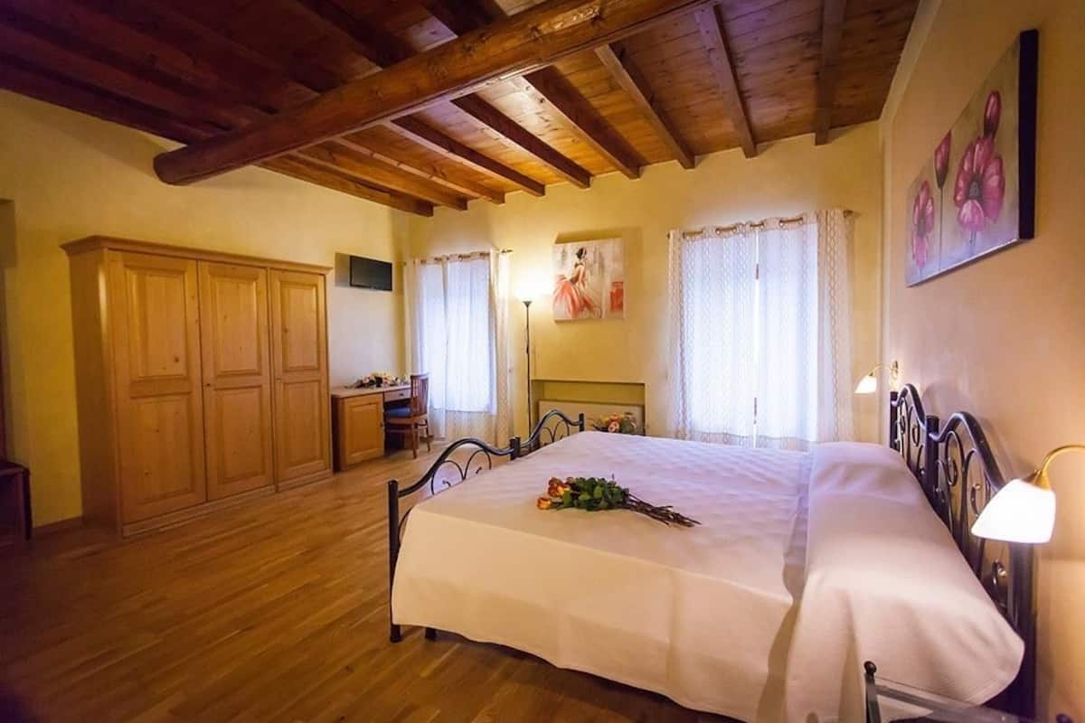 Un dormitorio con techo de madera, una cama con cubrecama blanco, una mesita de noche, un escritorio y un armario.