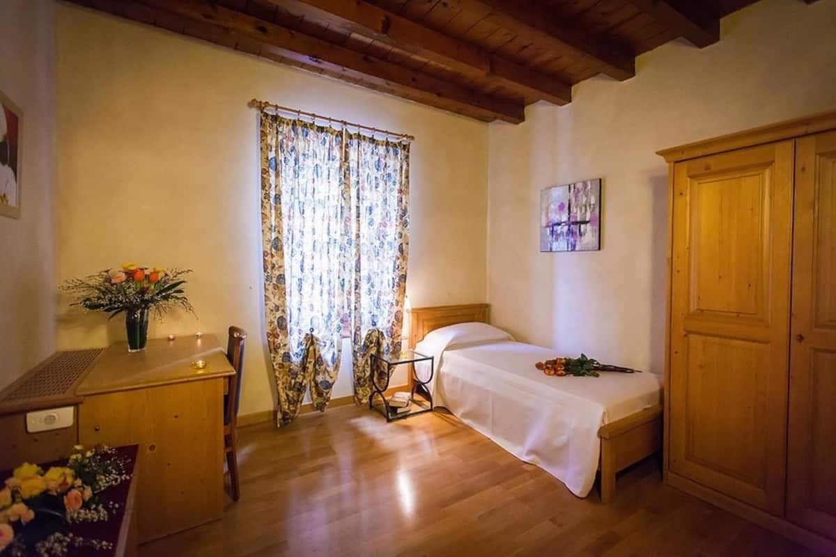 Un dormitorio con una cama de madera, un escritorio con un florero, una silla y un armario.