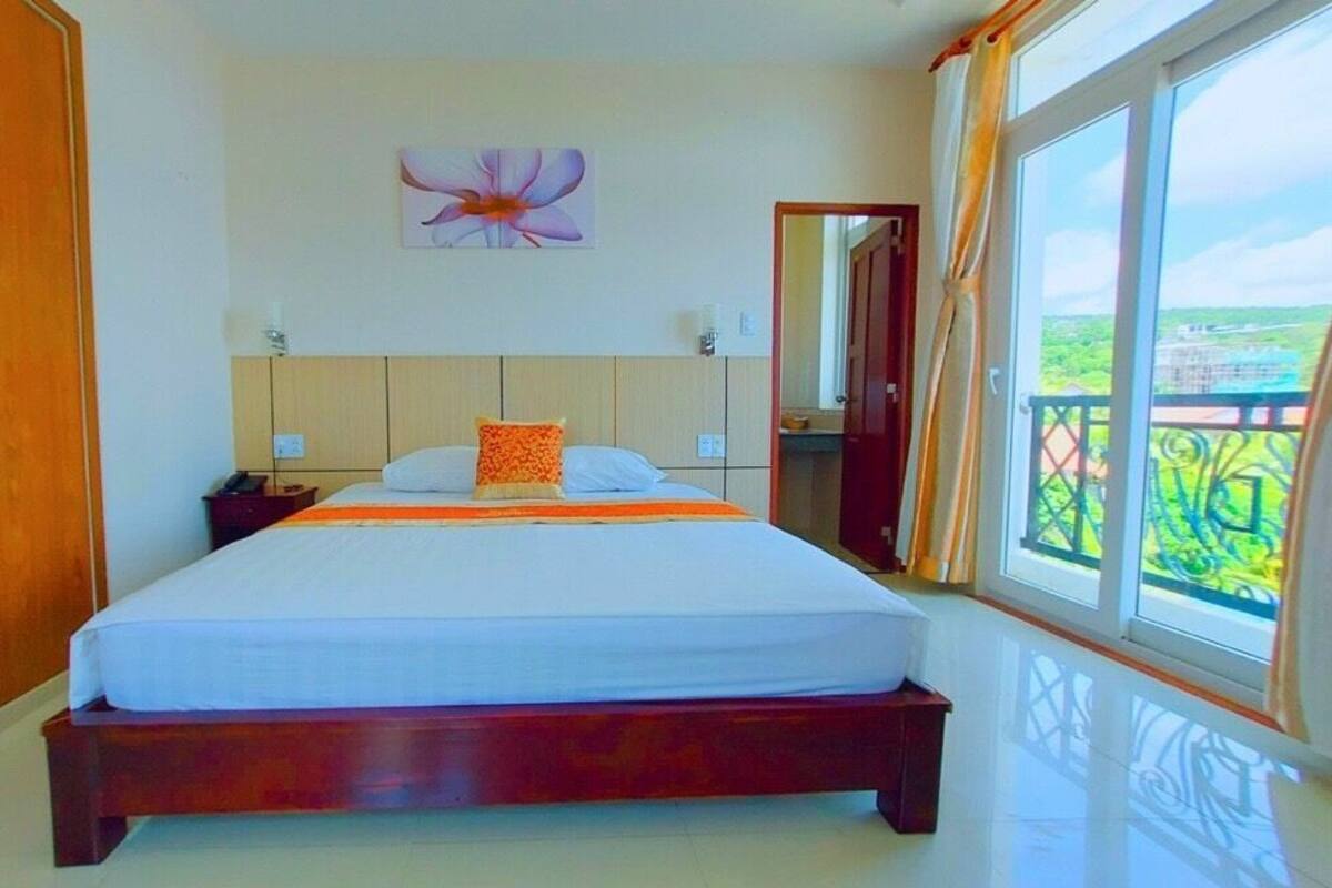 A bedroom with a large bed, wooden wardrobe, and a view through a window.
