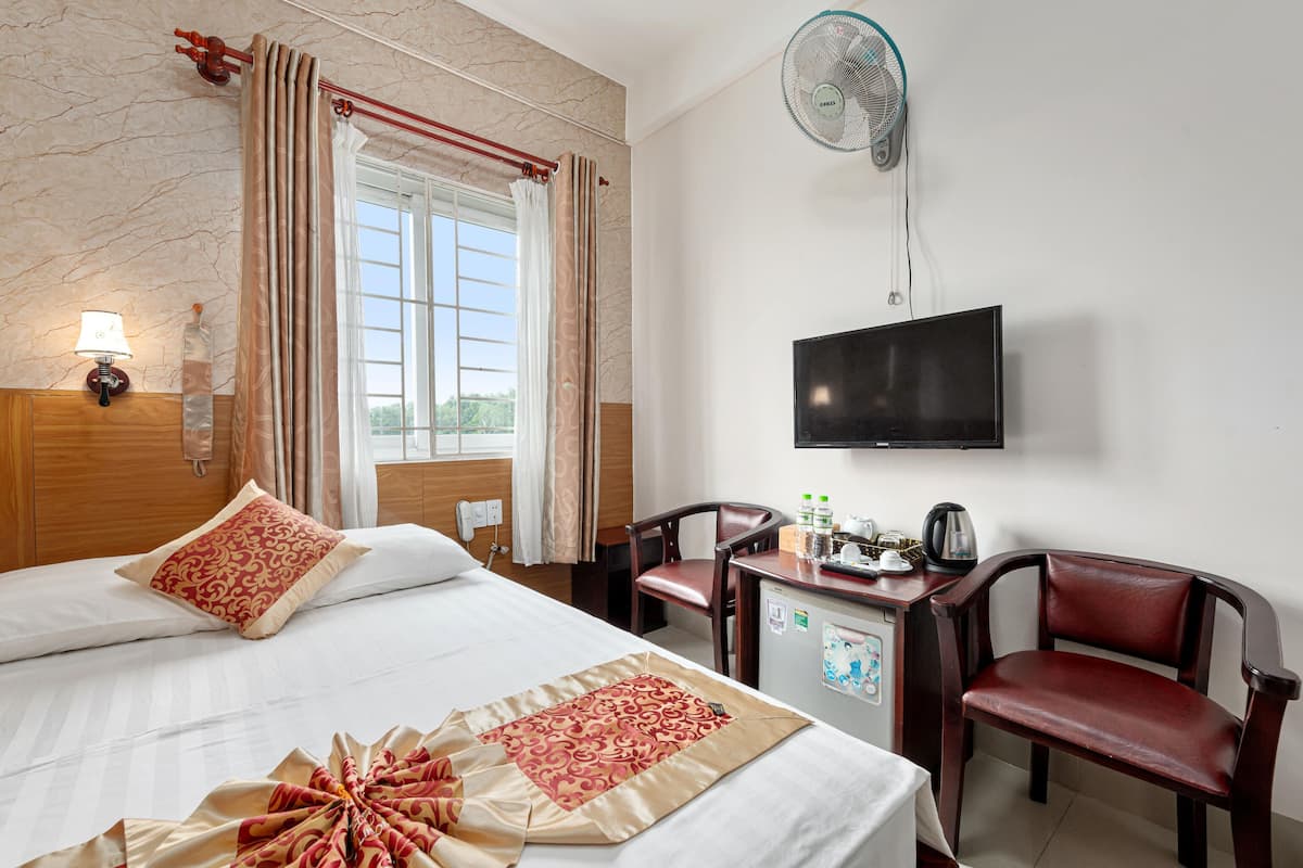 A hotel room with a bed, a desk, a chair, a television, and a fan.