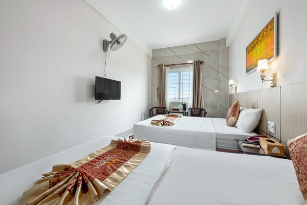 A hotel room with two beds, a flat-screen TV, a desk with a chair, a window with curtains, and a painting on the wall. - Victoria Phu Quoc Hotel (Phu Quoc)