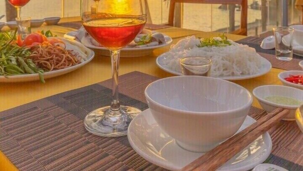 A table set for dinner with plates of food, a glass of red wine, and a bowl of rice. - Victoria Phu Quoc Hotel (Phu Quoc)