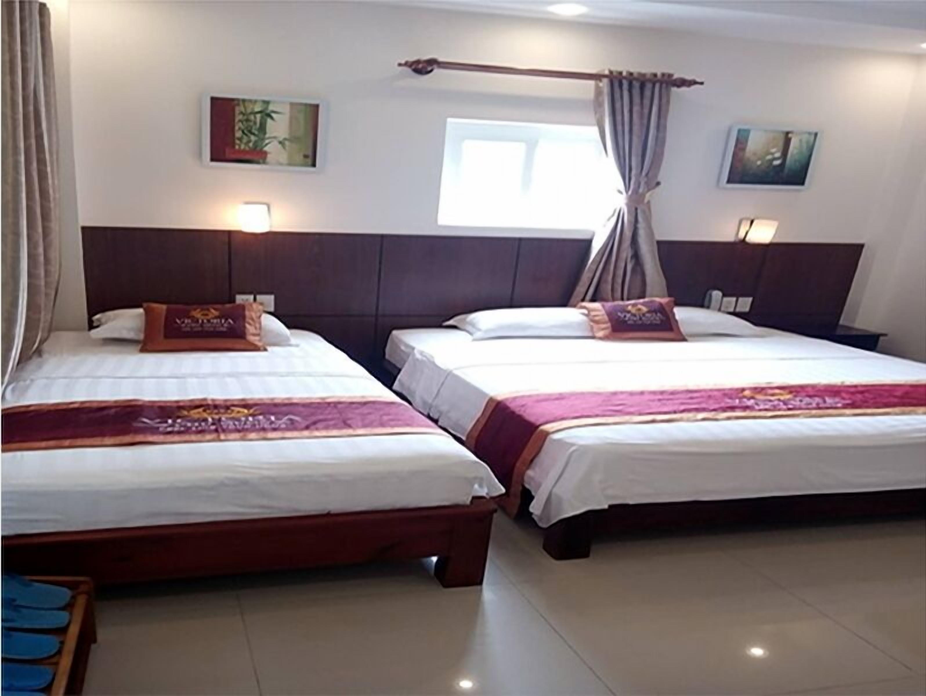 A hotel room with two beds, each with a headboard, a window with curtains, and wall-mounted lights.