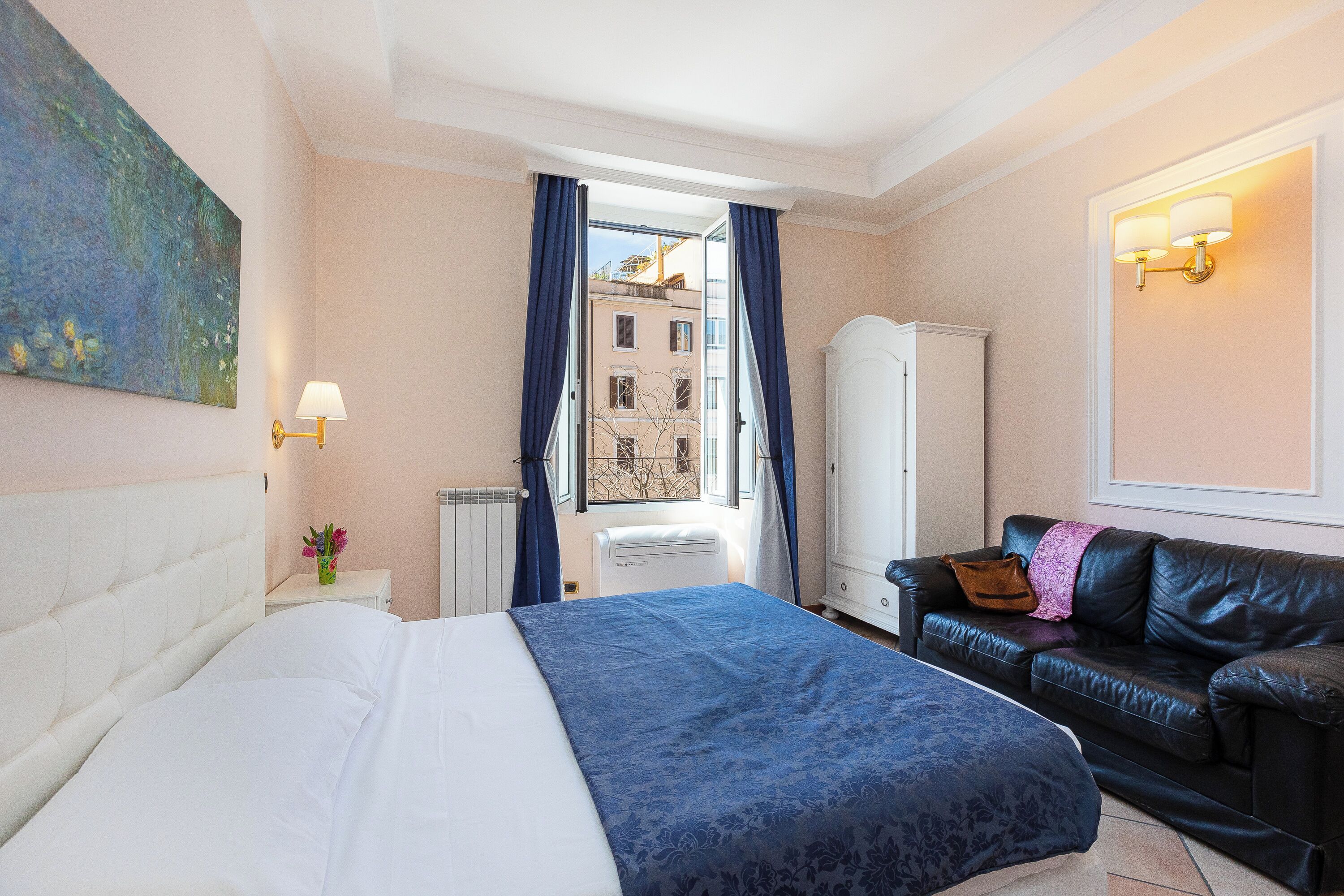 A hotel room with a bed, a black leather sofa, a white wardrobe, and a window with curtains.